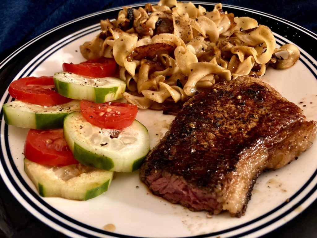 Steak, fried noodles, cucumber and tomato